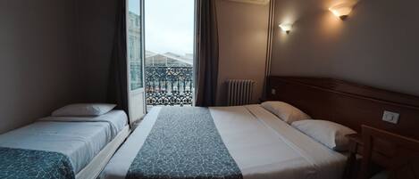 A hotel room with two beds, a window with curtains, an air conditioning unit, and a view of a building outside.