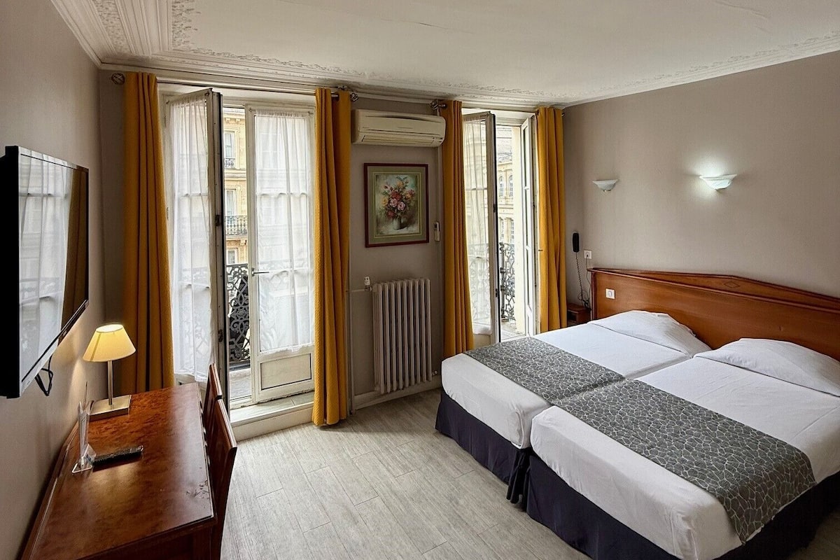 A hotel room with a bed, a desk, a chair, a lamp, and a window with curtains.
