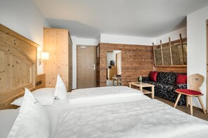 A hotel room with a wooden headboard, a bed with white linens, a sofa with red cushions, a small table, and a chair. - Hotel Digon (Castelrotto)