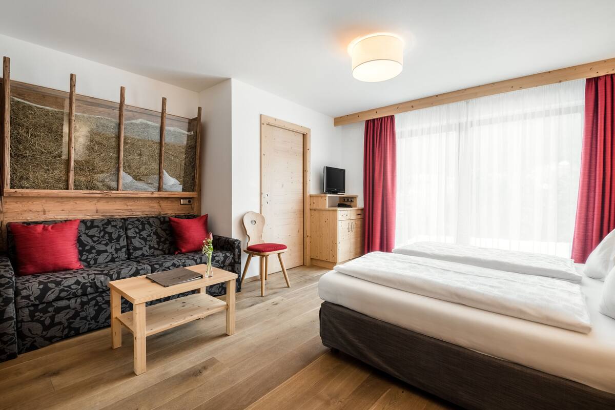 Una habitación de hotel moderna con suelo de madera, una cama, un sofá, un escritorio, una silla y un televisor.