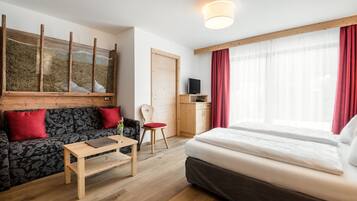 Ein modernes Hotelzimmer mit Holzboden, einem Bett, einer Couch, einem Schreibtisch, einem Stuhl und einem Fernseher.