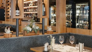 A restaurant with a wooden bar, cushioned seating, and wine bottles displayed on shelves. - Hotel Digon (Castelrotto)