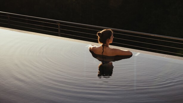 A person standing on a reflective surface with a view of a forest and mountains in the background. - Hotel Digon (Castelrotto)