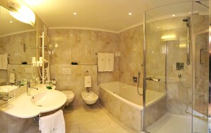A modern bathroom with a glass-enclosed shower, a freestanding bathtub, and a vanity with a sink and mirror. - Hotel Digon (Castelrotto)