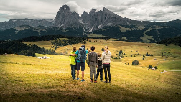 Un grupo de personas de pie en una colina cubierta de hierba con vistas a un paisaje montañoso bajo un cielo despejado.