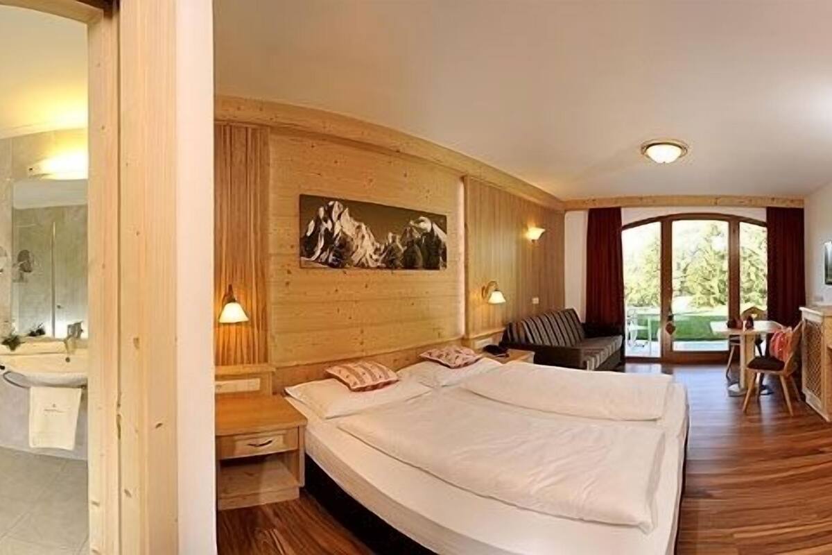 Un dormitorio con una cama grande, un cabecero de madera, un cuadro, un televisor y vistas al exterior.