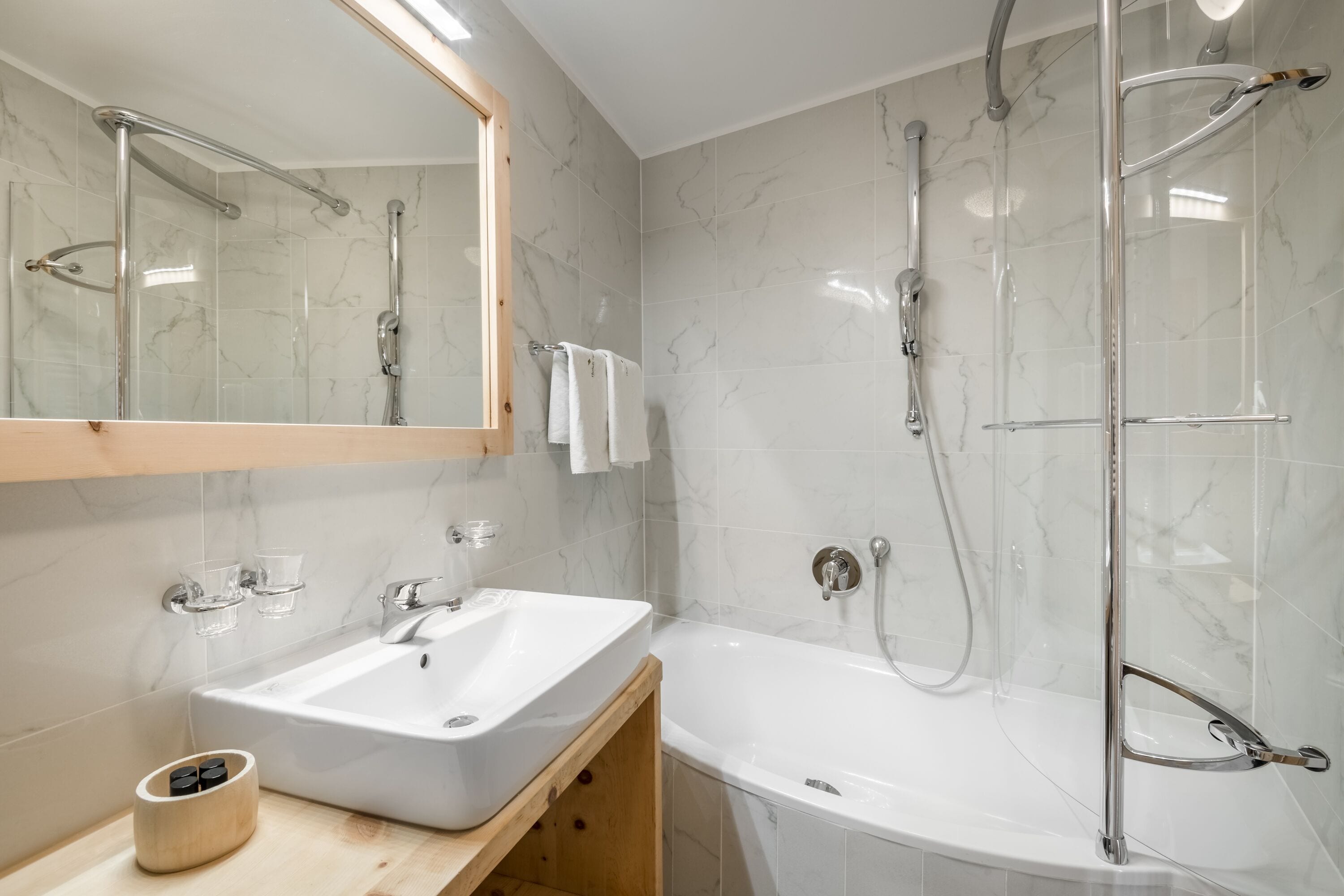 Un baño moderno con un lavamanos blanco, un espejo y una ducha con mampara de vidrio.