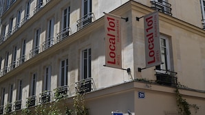 Un edificio con varias ventanas y balcones, cada uno con barandillas metálicas. Dos grandes lonas cuelgan de la esquina del edificio, anunciando 'Local 101 Hotel Beaurepaire'.