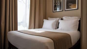 A hotel room with a large bed, beige curtains, and two framed pictures on the wall.
