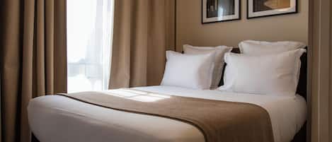 Une chambre d’hôtel avec un grand lit, des rideaux beiges et deux tableaux encadrés accrochés au mur.
