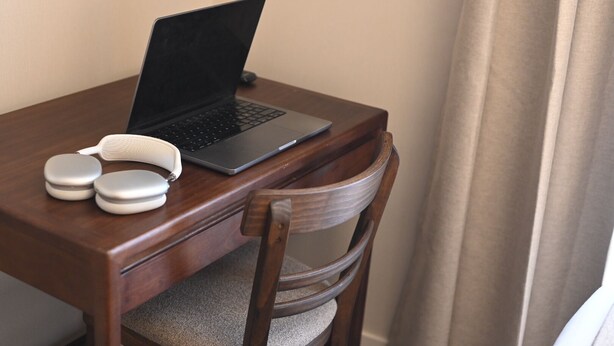 A laptop on a wooden desk with a chair, a pair of earphones, and a remote control.