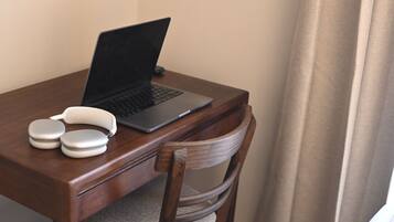 A laptop on a wooden desk with a chair, a pair of earphones, and a remote control.