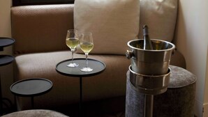 A cozy seating area with a cushioned bench, a small round table with two wine glasses, and a metal container on a stool. - Local 101 Beaurepaire (Paris)