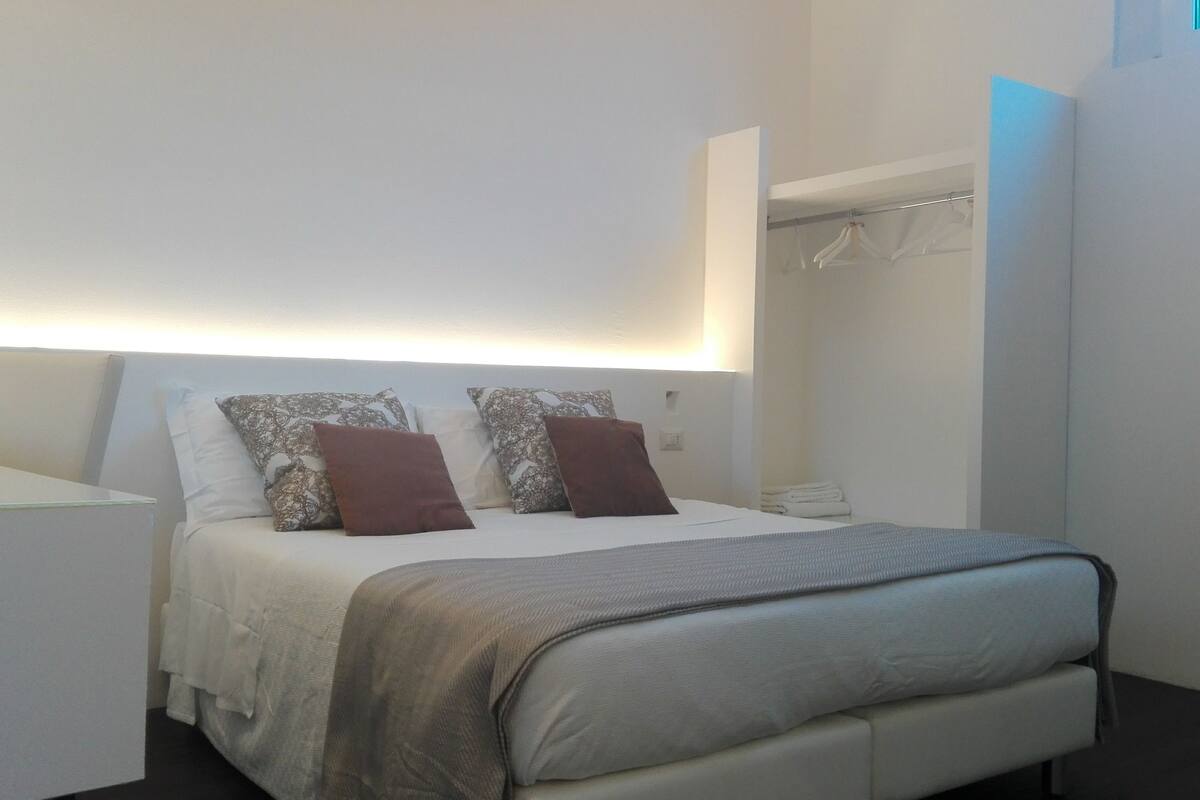 A modern bedroom with a bed, bedside tables, and a wardrobe.