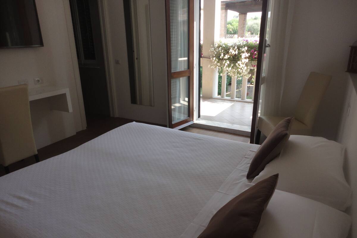 A hotel room with a bed, a desk, and a view of the outdoor balcony.