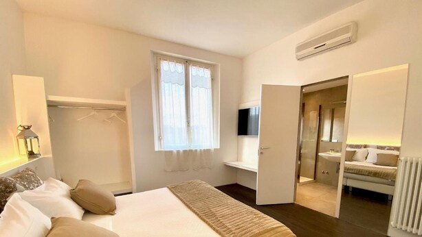 A bedroom with a bed, a bedside table, a TV, a wardrobe, and a bathroom visible through an open door. - Soggiorno Lo Stellino (Siena)