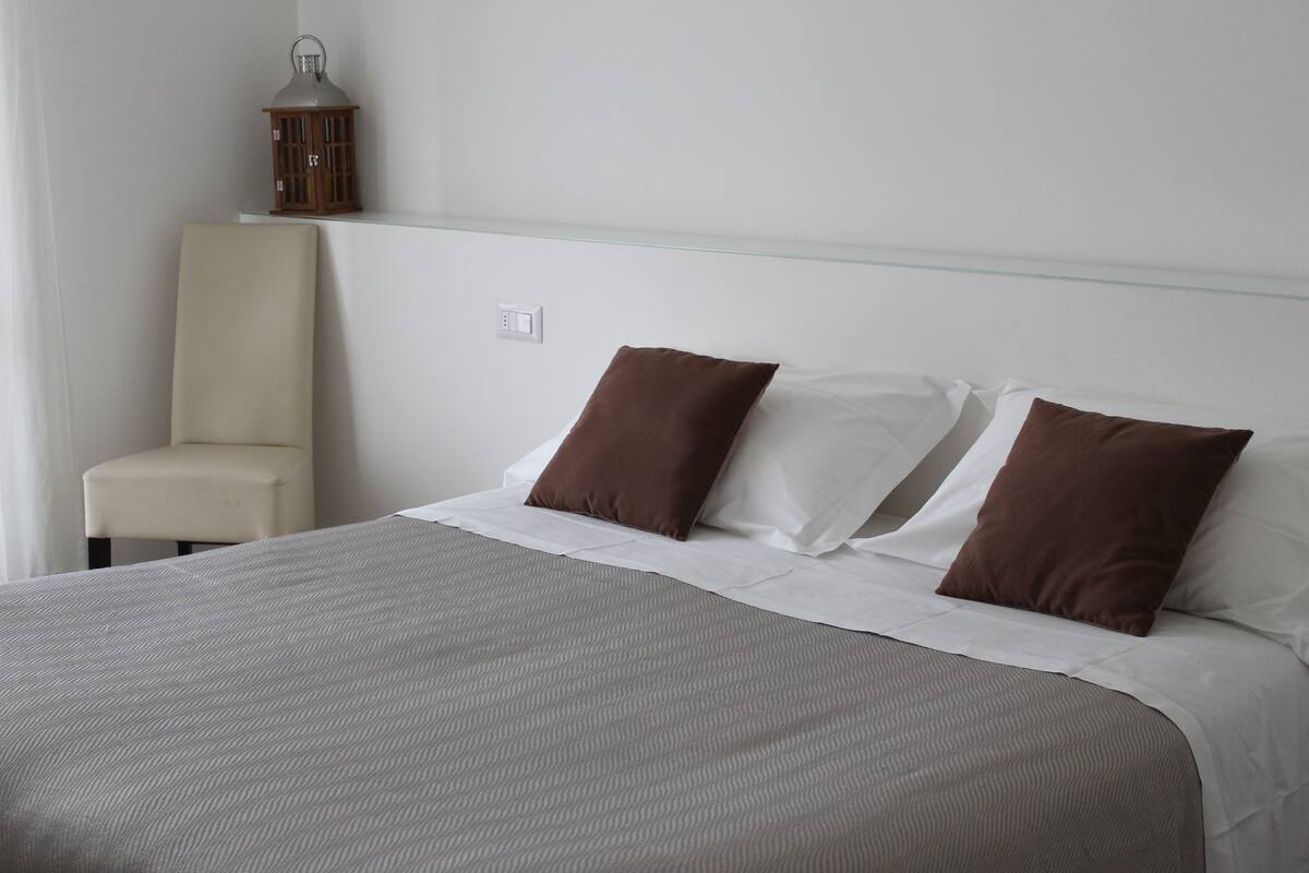 A neatly made bed with a grey and white striped bedspread, two brown pillows, and a white headboard.