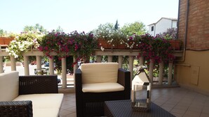A patio with wicker furniture, a white cushioned chair, and a table with a lamp. - Soggiorno Lo Stellino (Siena)