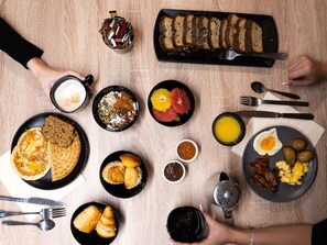 A breakfast spread with pancakes, eggs, sausages, and various fruits and pastries on a wooden table. - Mercure Paris Bastille Marais (Paris)