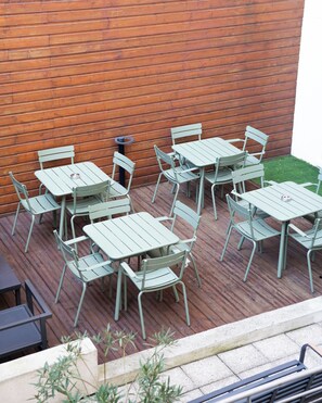 An outdoor patio with green metal tables and chairs, a wooden wall, and a small patch of grass. - Mercure Paris Bastille Marais (Paris)