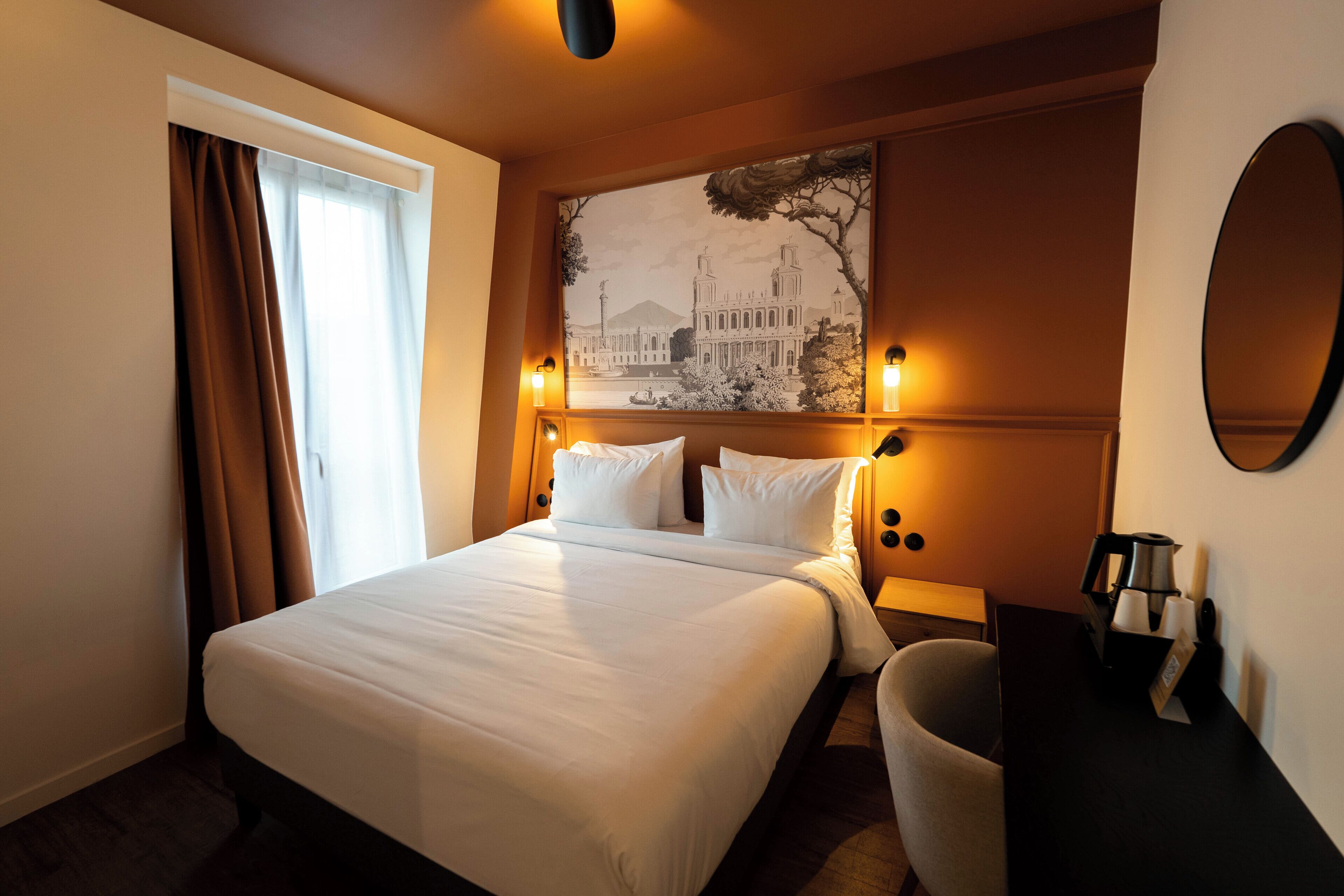 Une chambre d’hôtel avec un grand lit, un bureau avec une lampe, une chaise et un miroir fixé au mur.