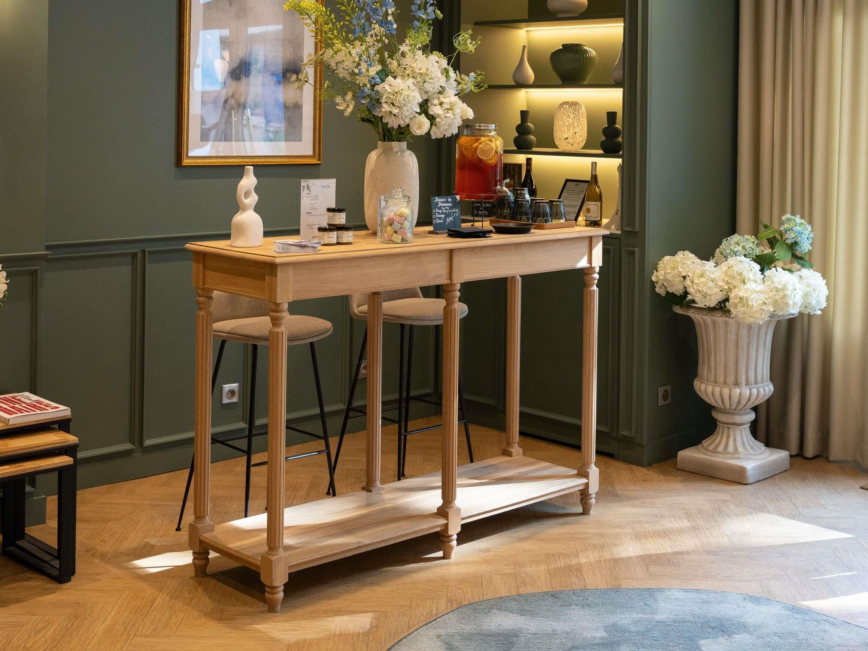 A wooden bar table with stools, a vase with flowers, and various bottles and glasses.