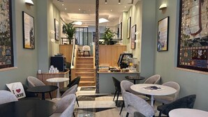 Un café moderno con mesas y sillas redondas, una escalera que lleva a un nivel superior y obras de arte en las paredes.