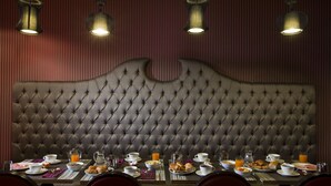 A dining area with a tufted headboard, a table set with breakfast items, and pendant lighting. - Hôtel du Prince Eugène (Paris)