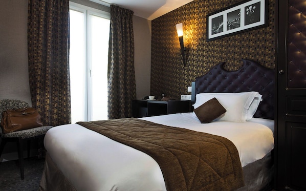 A hotel room with a large bed, a nightstand, a chair, and a window with curtains. - Hôtel du Prince Eugène (Paris)
