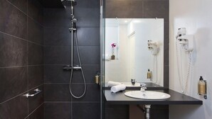 A modern bathroom with a dark tiled shower, a white sink, and a large mirror. - Hôtel du Prince Eugène (Paris)