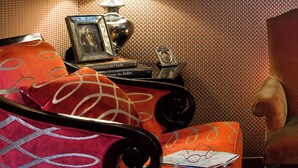 A hotel room with a bed, a nightstand with books and a lamp, and patterned wallpaper. - Hôtel du Prince Eugène (Paris)