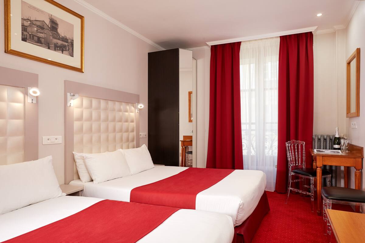 A hotel room with two beds, a wooden desk, a chair, and a red carpet.