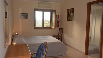 A bedroom with a bed, a desk, a chair, a window, and a door.