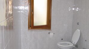 A bathroom with a toilet, a window, and tiled walls. - Agriturismo Torre Del Golfo (Cropani)