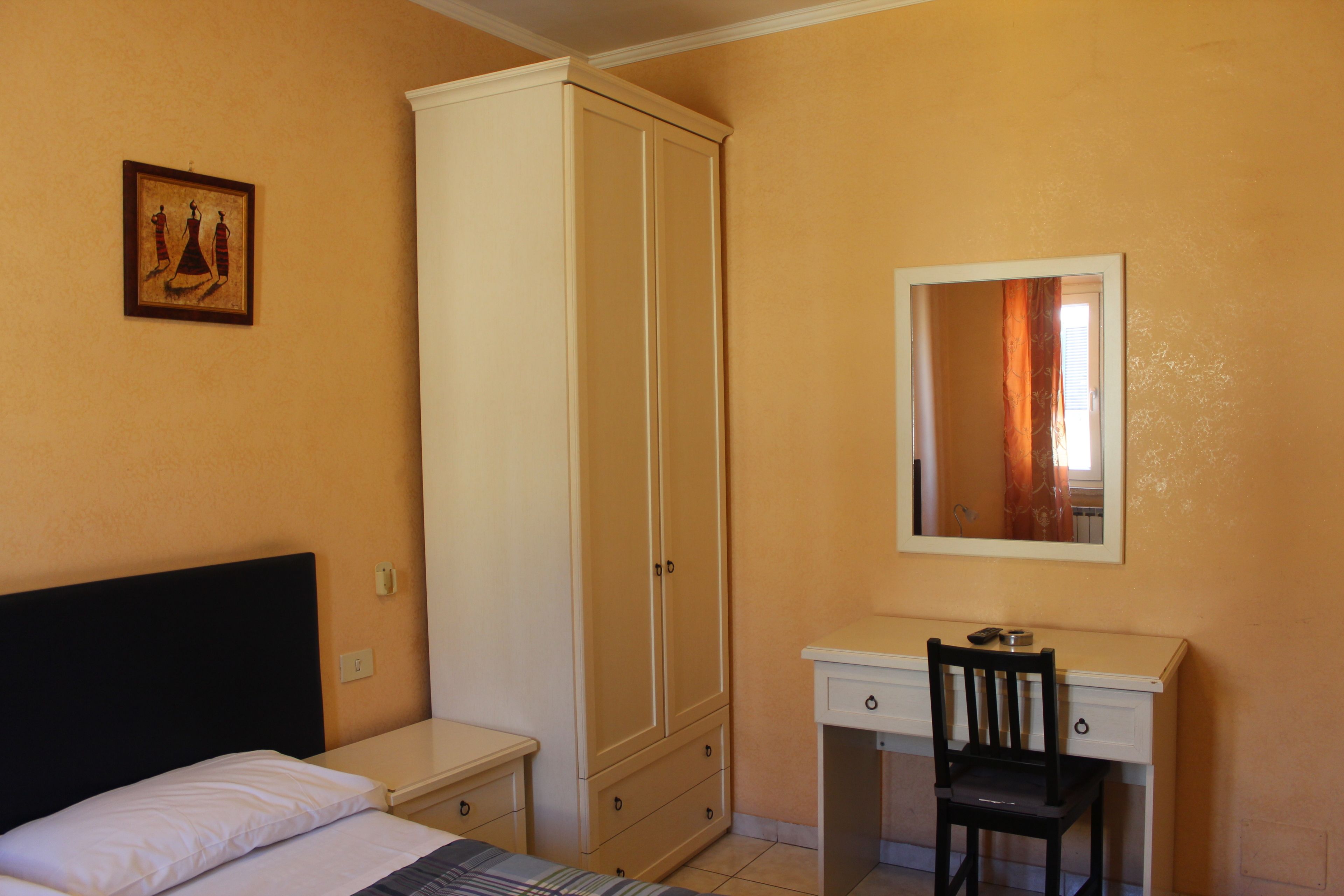 A bedroom with a bed, a wardrobe, a desk with a chair, and a mirror.