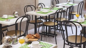 A dining area with tables set for breakfast, including croissants, juice, and newspapers. - Hôtel de la Place des Alpes (Paris)