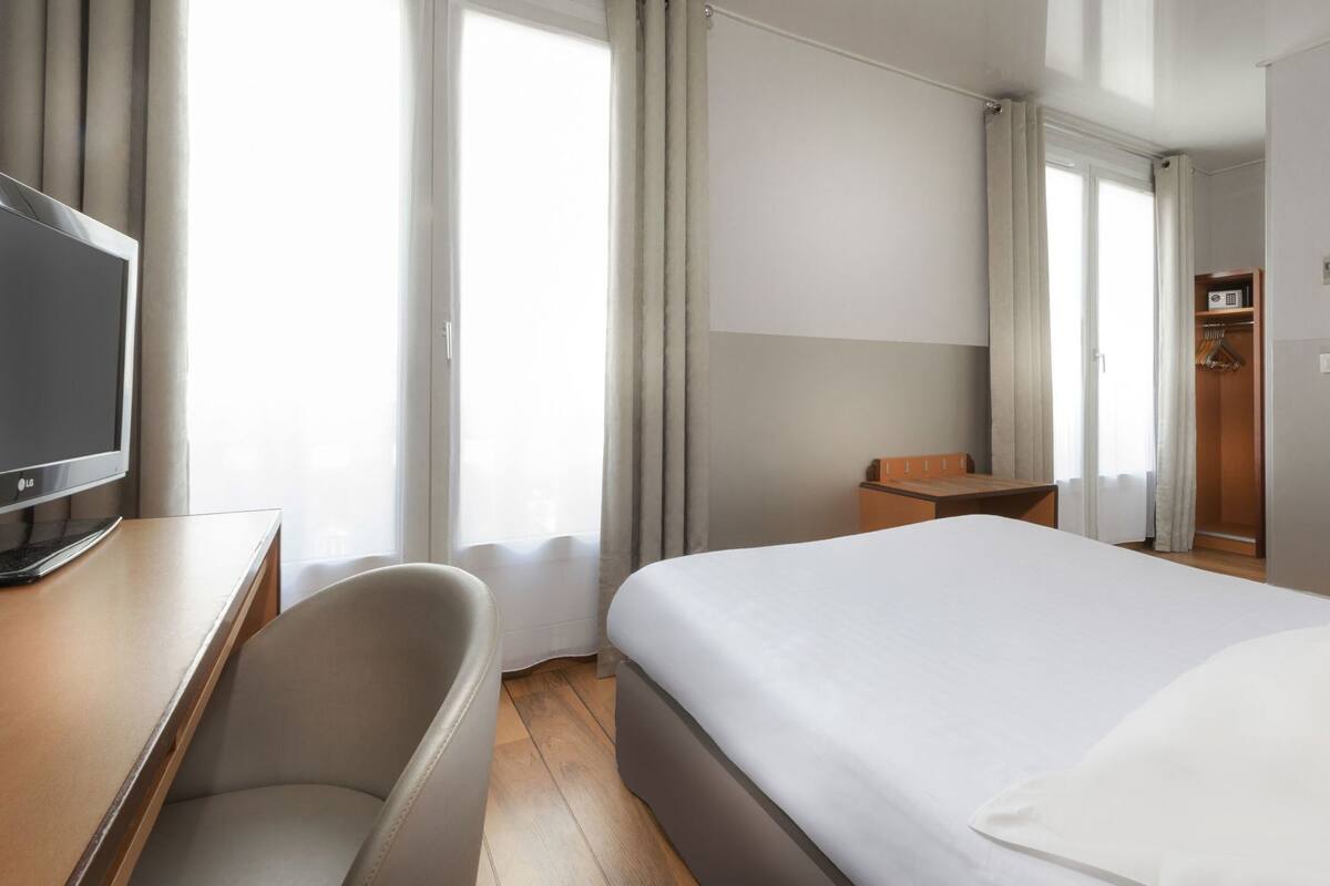 Hotellihuone, jossa on sänky, työpöytä, tietokone, tuoli ja televisio.