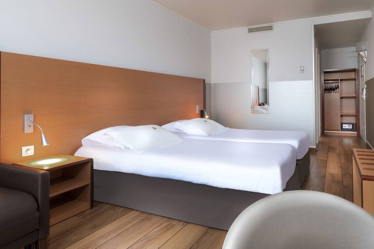 Hotellihuone, jossa on suuri sänky, yöpöydät, tuoli, vaatekaappi ja peili.