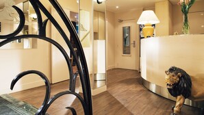 A hotel lobby with a reception desk, a mirror, a staircase, and a lion statue. - Hôtel du Lion (Paris)