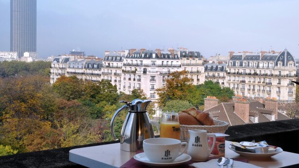 A breakfast setup with a coffee pot, cups, and pastries on a balcony overlooking a cityscape with historic buildings and a modern skyscraper. - Hôtel du Lion (Paris)