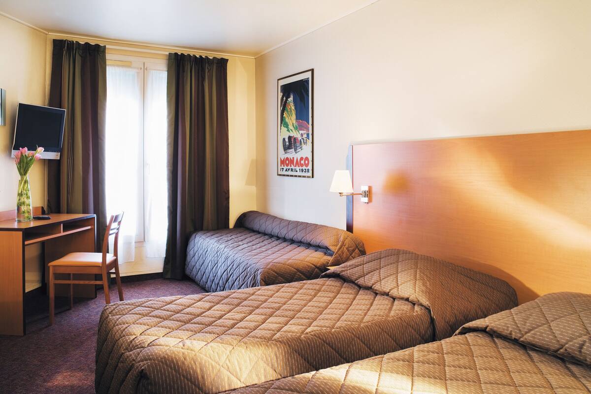 Hotellihuone, jossa on kaksi sänkyä, työpöytä, tuoli, televisio ja juliste seinällä.