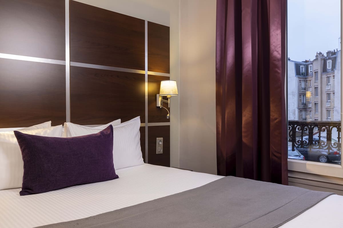 Une chambre d’hôtel avec un grand lit, une table de chevet avec une lampe et une vue sur la ville par la fenêtre.