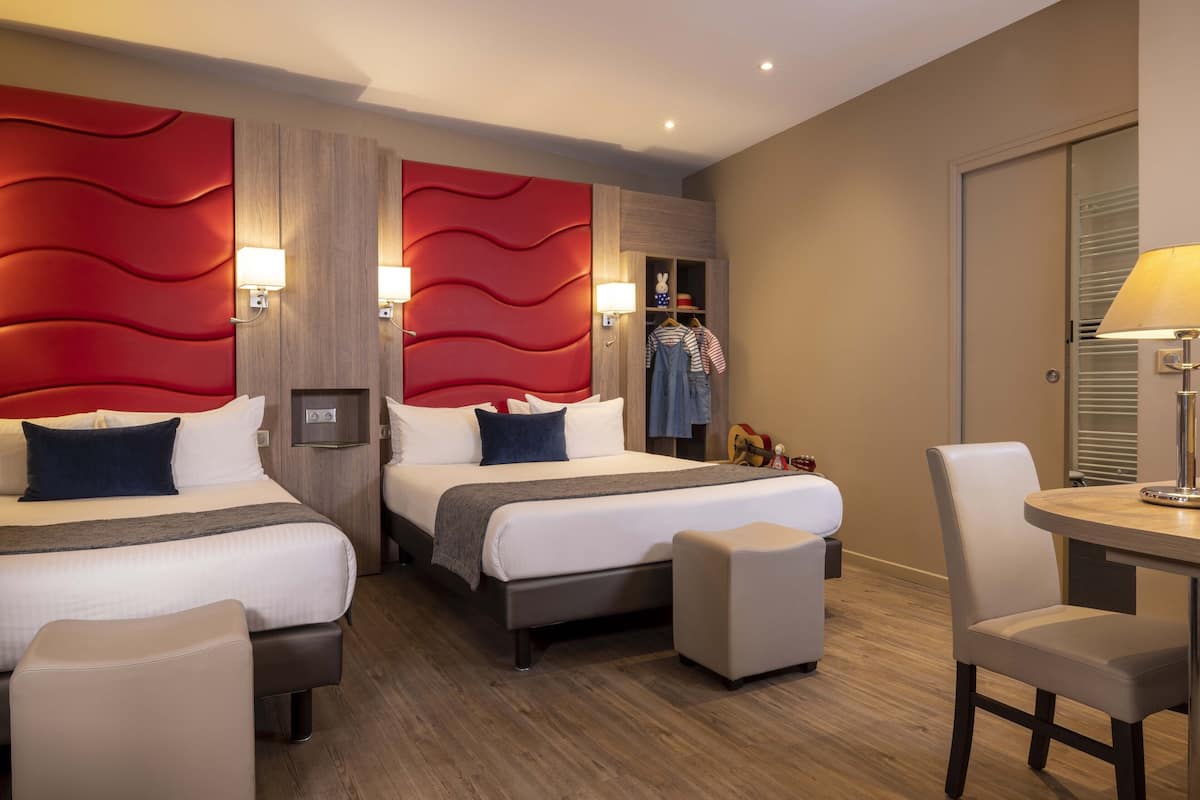 Une chambre d’hôtel avec deux lits, un coin repas et un placard avec un miroir.