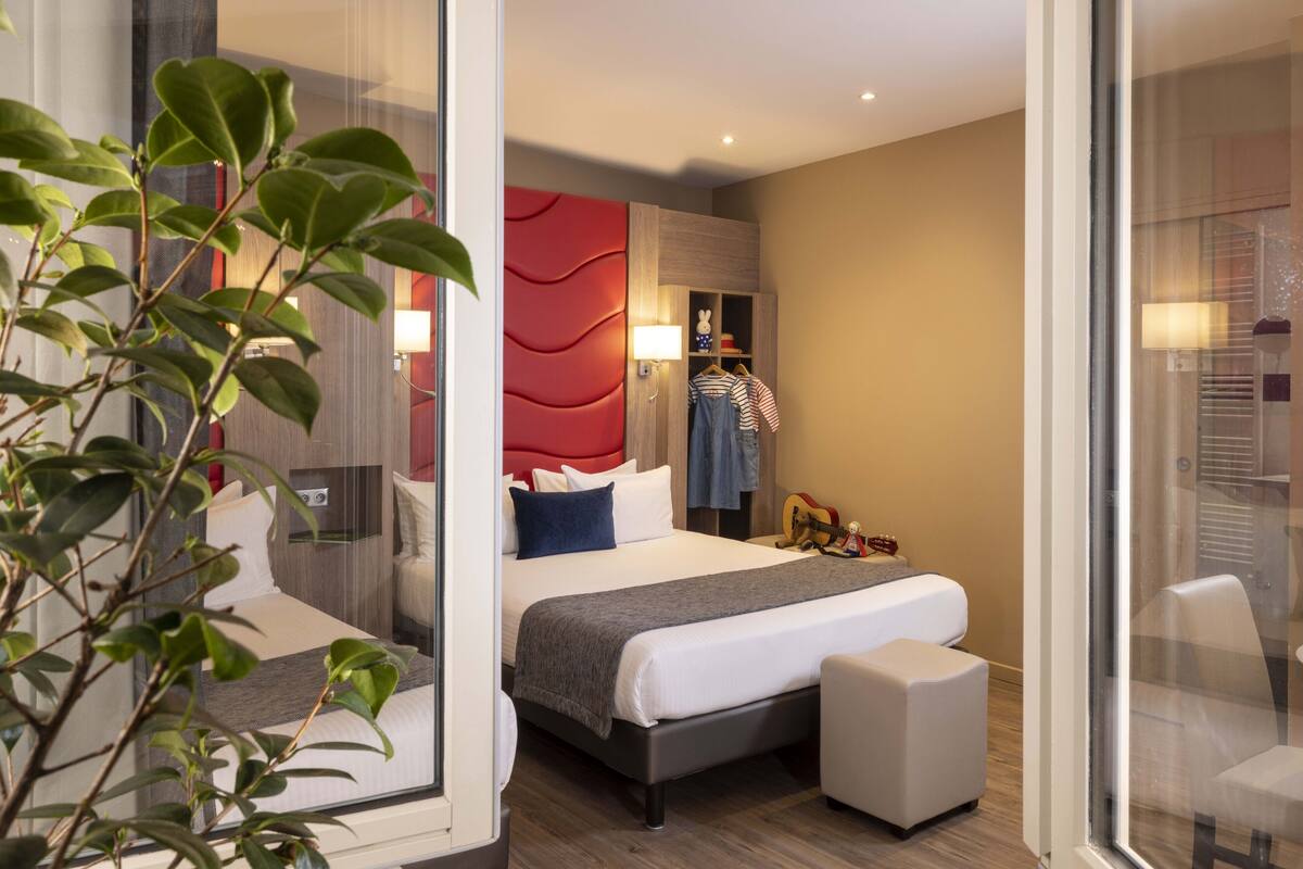 Une chambre d’hôtel moderne avec un grand lit, une table de chevet, un petit coin salon et une armoire.