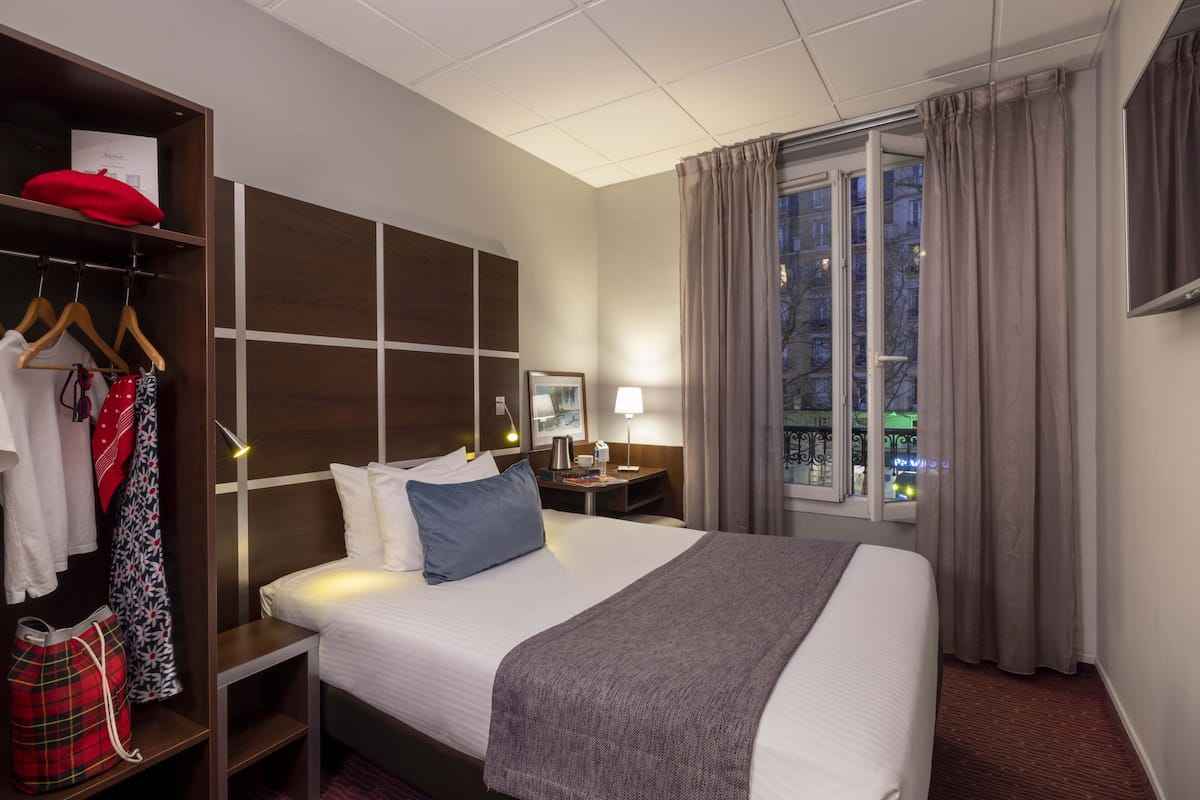 Une chambre d’hôtel avec un lit, des tables de chevet, une armoire et une fenêtre avec des rideaux.