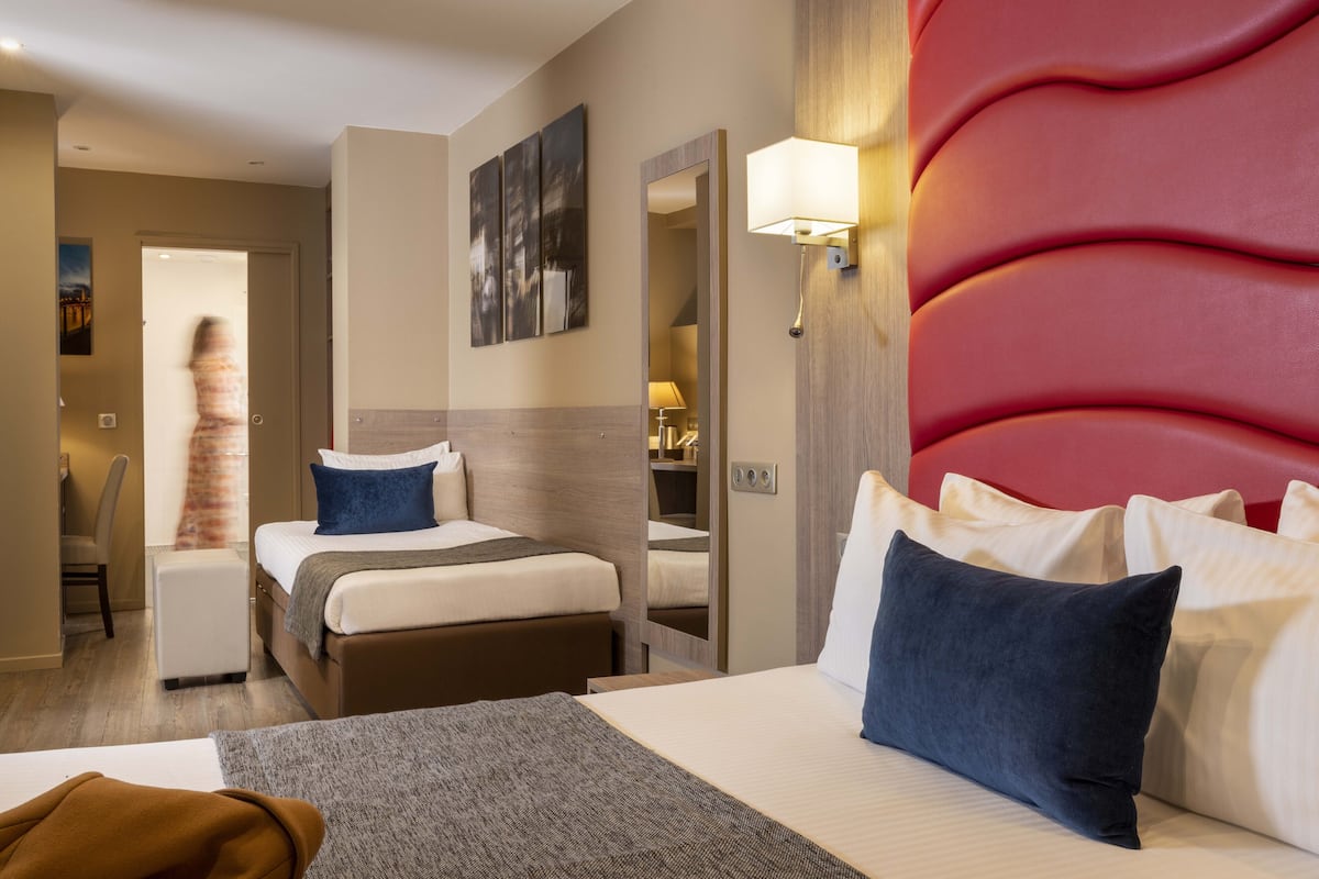 Une chambre d’hôtel avec deux lits, un coin salon, un miroir et un mur d’accent rouge.