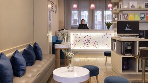 A hotel reception area with a sofa, round tables, a reception desk, and a TV screen.