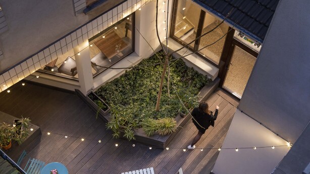 An outdoor patio area with a wooden deck, string lights, and a small garden.