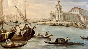 Cena histórica à beira-mar com barcos, um edifício imponente com torre e uma ponte.