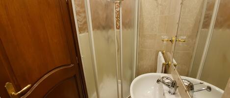 Ein Badezimmer mit Holztür, Duschkabine aus Glas, Waschbecken mit Spiegel und beige gefliesten Wänden.